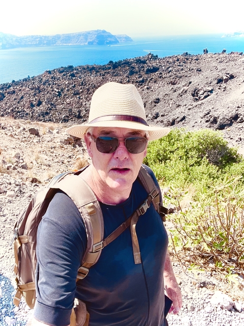       Man outdoors wearing a hat and sunglasses, with a rocky landscape in the background.
  