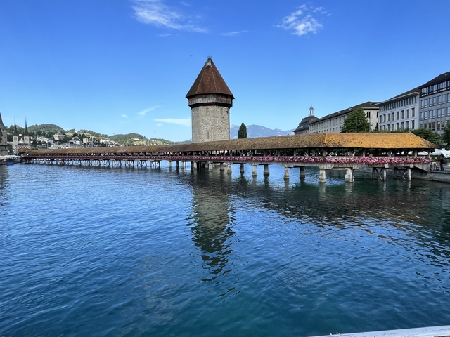       Historic wooden bridge with flowers crossing a body of water.
  