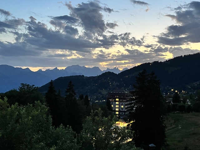       Sunset over a valley with silhouettes of trees and mountains.
  
