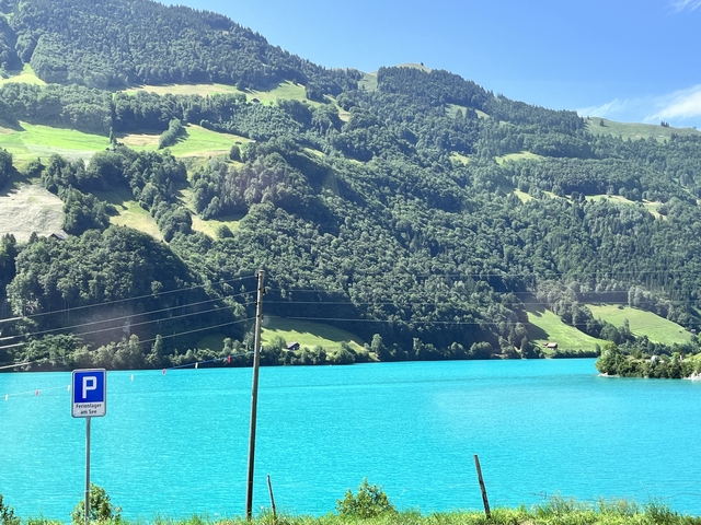       Vivid blue lake with hilly backdrop and a parking sign.
  