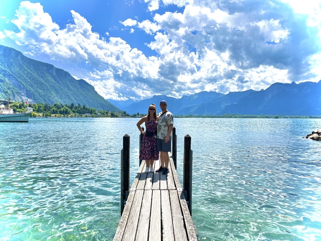      Couple on a dock with mountains and cloudy sky in the background.
  
