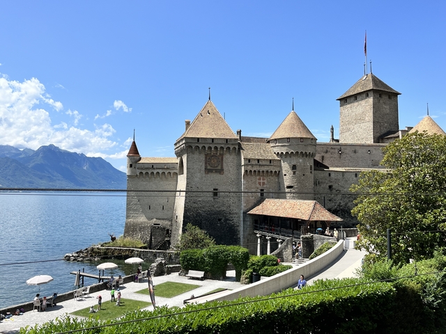       Chillon Castle by a lake with mountainous backdrop.
  
