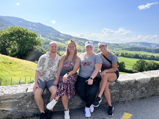      Friends sitting on a stone wall with a scenic landscape.
  