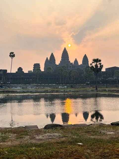 An ancient temple reflecting in a pond with the sun setting.