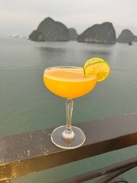 A cocktail glass with a lime on a balcony railing overlooking the sea.