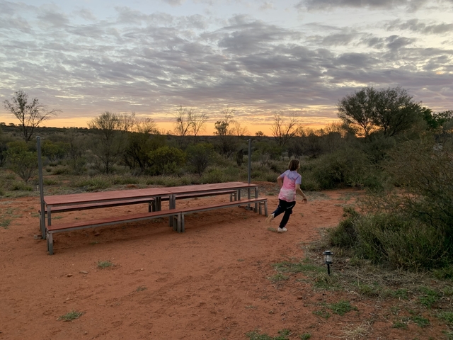 Child running near picnic tables in a desert landscape at sunset.