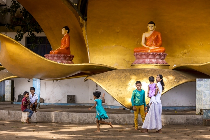 Children playing near golden sculptures of the Buddha.