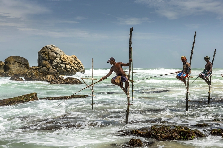 Fishermen on stilts by the ocean.