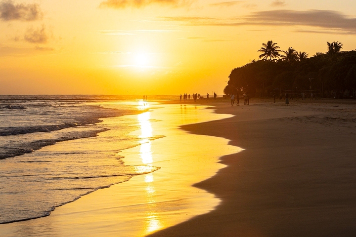 A beautiful sunset on a sandy beach with silhouettes of people.