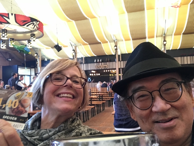 Two smiling people at a festive indoor setting with tables and signs.