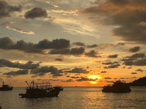       Sunset over the ocean with boats silhouetted against the horizon.
  