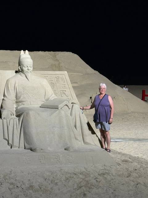 A woman standing next to a sand sculpture at night.