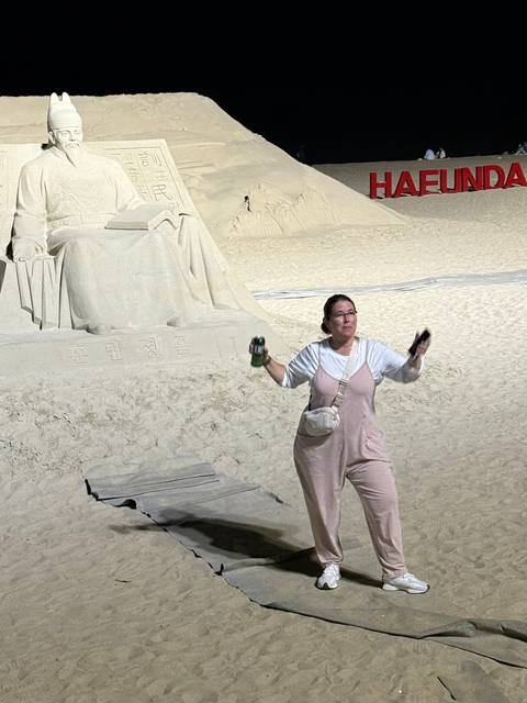 A woman posing with a sand sculpture at night.