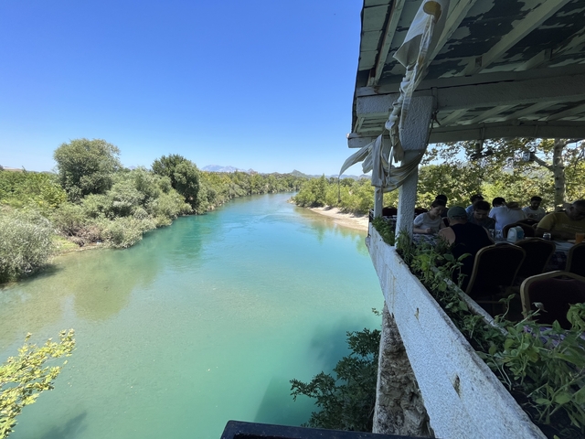      People dining at a restaurant by the river.
  