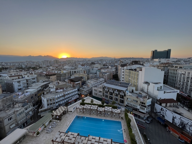       Cityscape at sunset with buildings and a pool in the foreground.
  