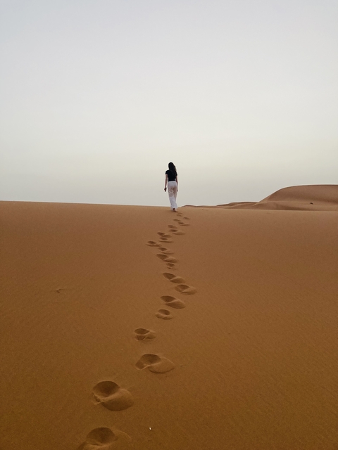       Person walking on sand dunes leaving footprints.
  