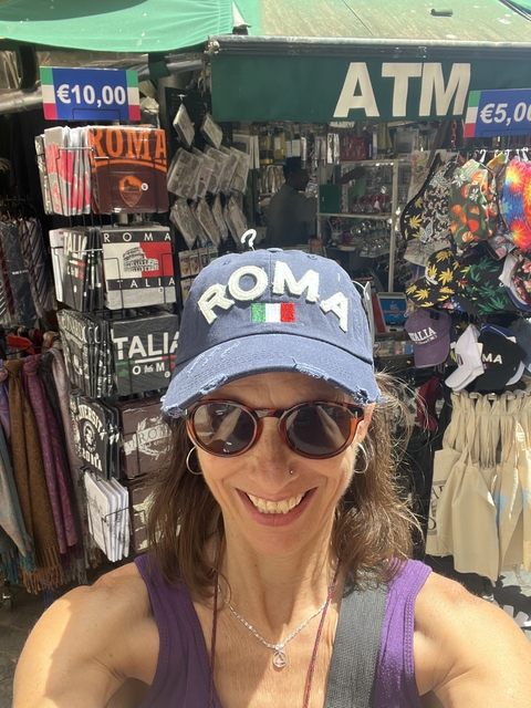 Person wearing a cap inscribed with 'ROMA' in a souvenir shop.