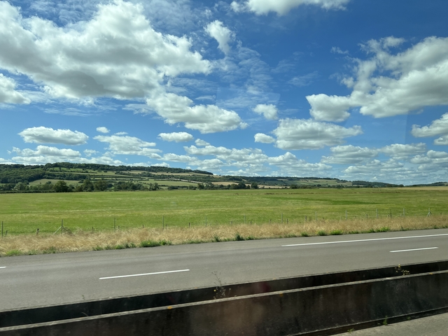       Rolling countryside with fields and scattered clouds.
  