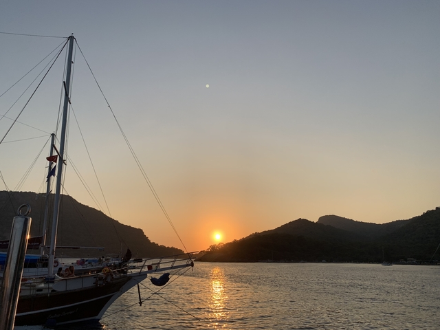       Sunset over a serene bay with a sailboat.
  