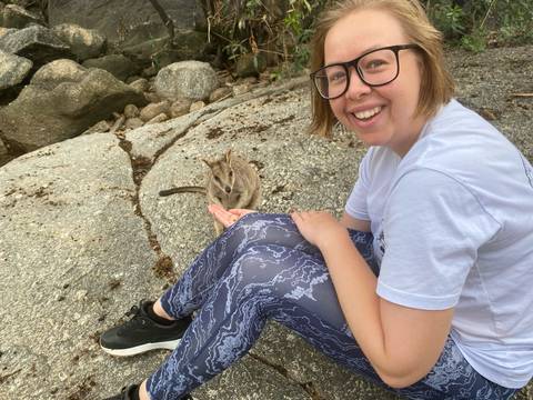       Smiling person petting a small animal on a rocky surface.
  