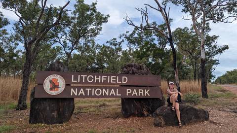       Person sitting by a sign for Litchfield National Park.
  