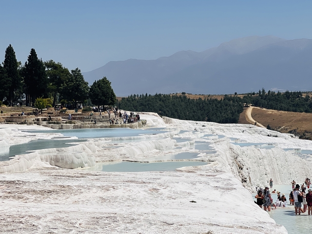       Terraced pools of white mineral deposits with people exploring.
  