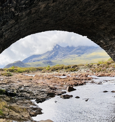 Rocky riverbed under an arch bridge with mountain scenery.