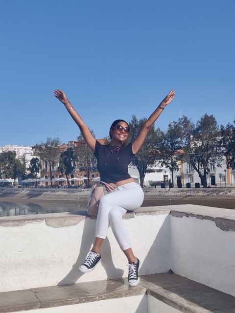       Woman joyfully posing on a stone bench by a river.
  