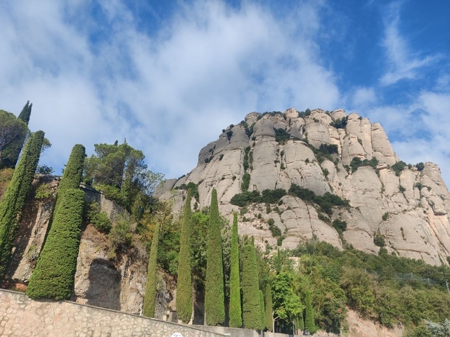       Rocky cliffs against a blue sky with scattered clouds.
  