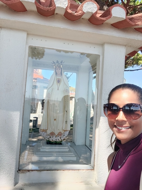       Woman posing next to a religious statue behind glass.
  