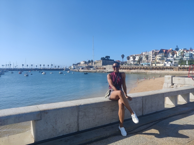       Woman sitting on a stone railing by a beach.
  