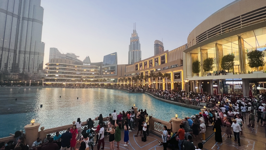       Crowded area with a large pond and illuminated buildings.
  