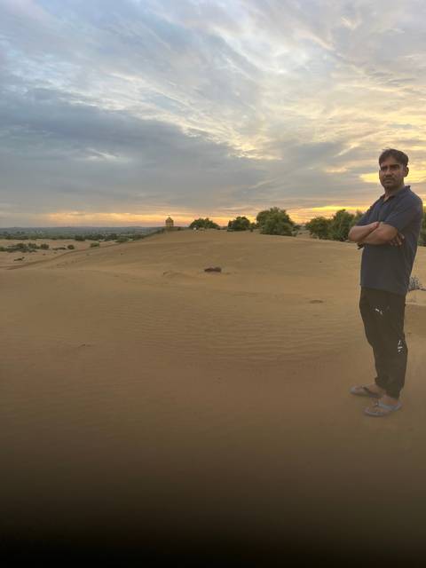      Person standing on a sandy landscape at sunset.
  