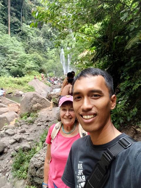       People in front of a waterfall in a forest setting.
  