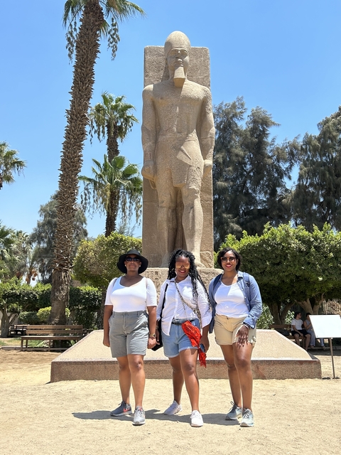 Three people posing in front of a large statue in a garden.