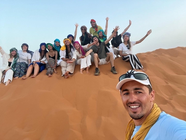 Group of people posing on sand dunes wearing colorful veils.