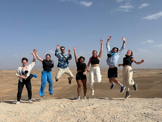Seven people jumping in a desert landscape.