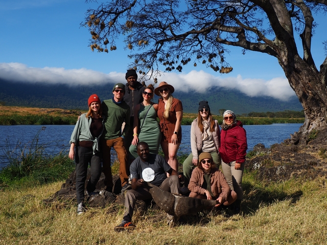       Group of people posing by a lake with mountains.
  