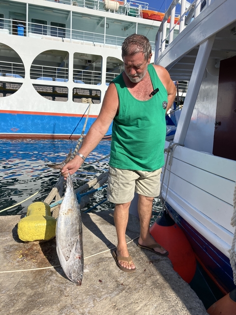       Person holding a large fish by a boat in a marina.
  