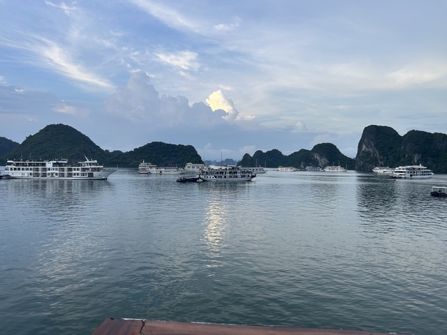 Limestone karsts and cruise ships on tranquil water at Halong Bay.