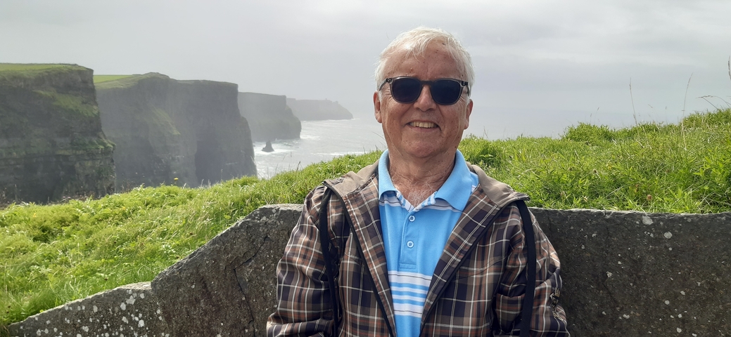 Man in front of Cliffs of Moher with ocean and grassy cliffs in background.
