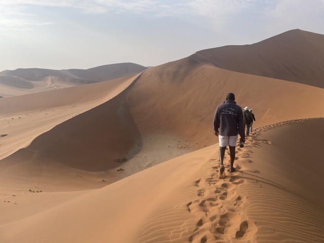 People hiking along a ridge of towering sand dunes.