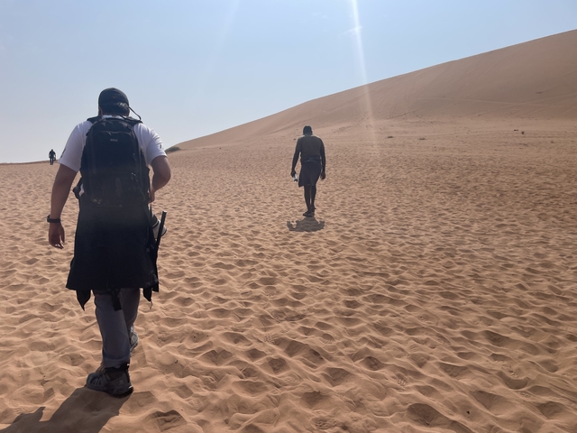 People walking on a sand dune under a clear sky.