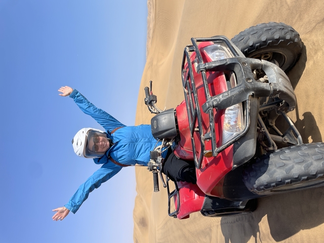 Person riding an ATV on sand dunes with arms raised.