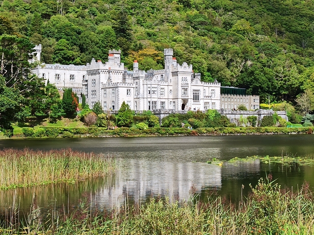 Kylemore Abbey reflecting in a calm lake surrounded by trees.
