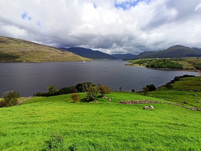 Scenic view of a lake surrounded by rolling hills and clouds.