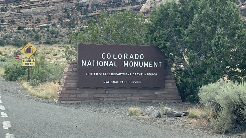 Entrance sign for Colorado National Monument surrounded by vegetation.
