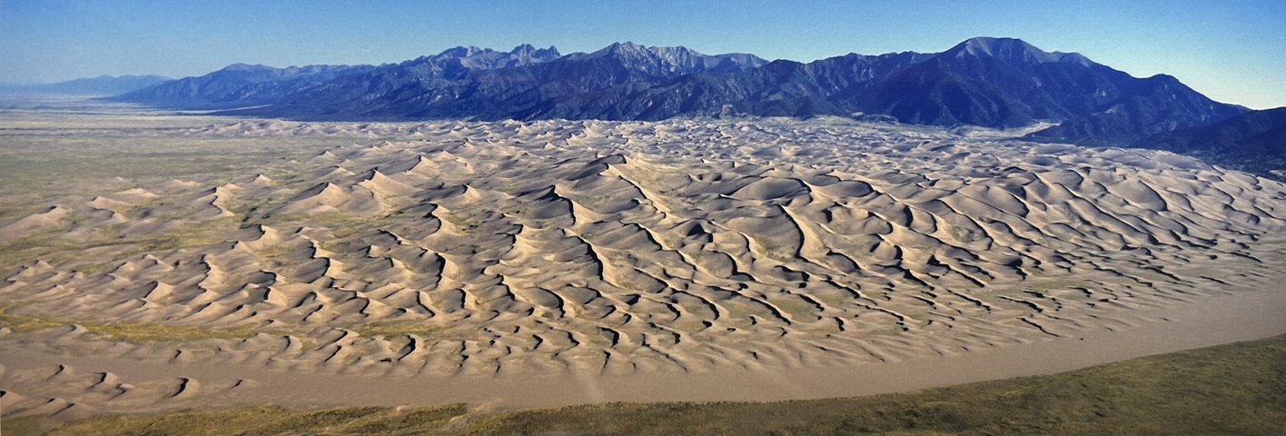       Expansive view of sand dunes with a mountain range in the background.
  