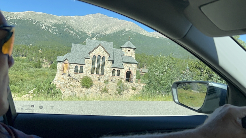       Chapel on the right viewed from inside a car with mountains in the background.
  