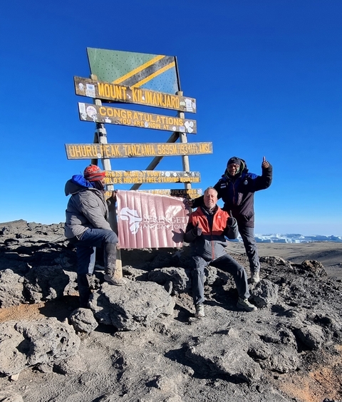 People posing with a sign at the summit of Uhuru Peak.